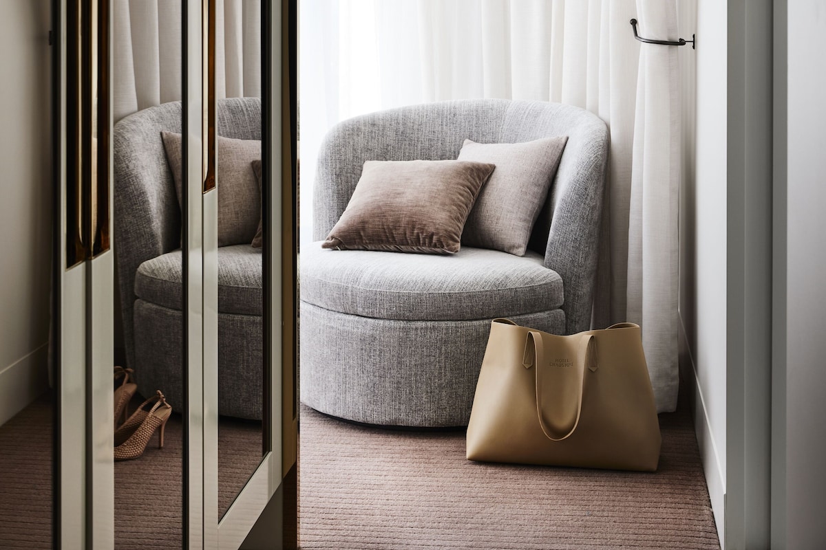Et moderne værelse med en grå sofa, en beige håndtaske og et spejl der reflekterer rummet.