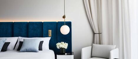 A modern hotel room with a large bed, a bedside table with a vase of flowers, a round table with a phone, and a chair.