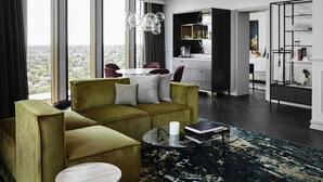 A modern living room with a green sofa, a round coffee table, and a view of the city through large windows. - Hotel Chadstone Melbourne MGallery Collection (Chadstone)