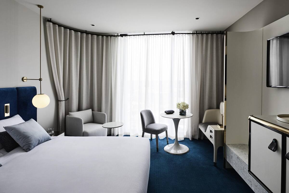 A hotel room with a large bed, a desk, a chair, a small table with a vase, and a television.