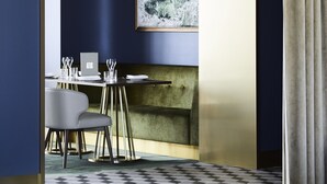 A modern dining area with a high-backed chair, a table set with plates and glasses, and a large window with a view of trees. - Hotel Chadstone Melbourne MGallery Collection (Chadstone)