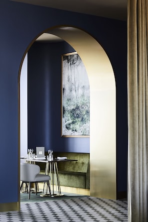 A modern dining area with a high-backed chair, a table set with plates and glasses, and a large window with a view of trees.