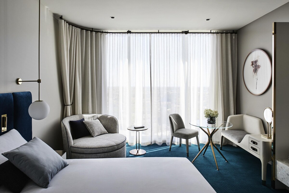 A modern hotel room with a large bed, a sofa, a small round table, and a chair.
