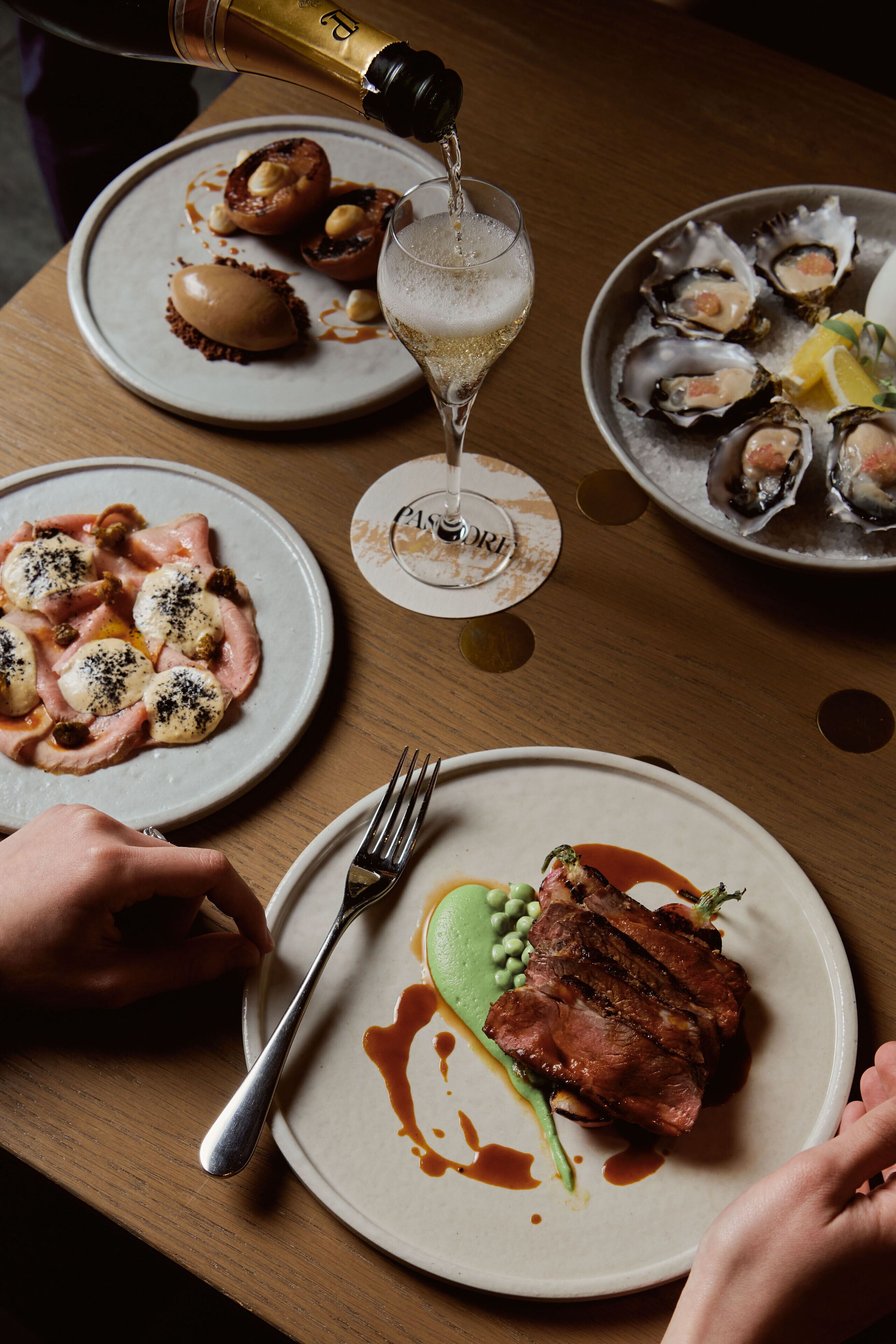A dining table with plates of food, a bottle of champagne, and a glass of wine.