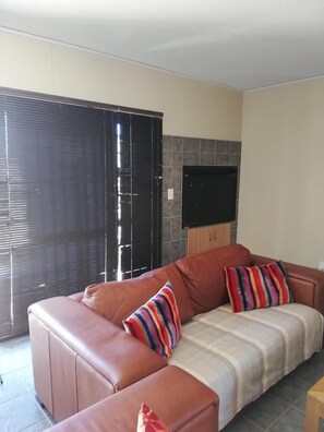 A living room with a brown leather sofa, striped pillows, and a television mounted on the wall.