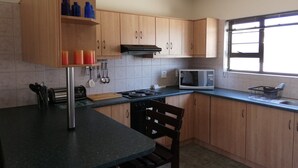 A kitchen with wooden cabinets, a microwave, a stove, and a window with blinds. - On The Dunes 8 (Henties Bay)