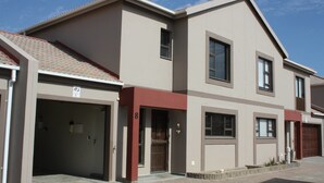 A modern two-story residential building with a garage on the ground floor, a small balcony on the second floor, and a red-tiled roof. - On The Dunes 8 (Henties Bay)