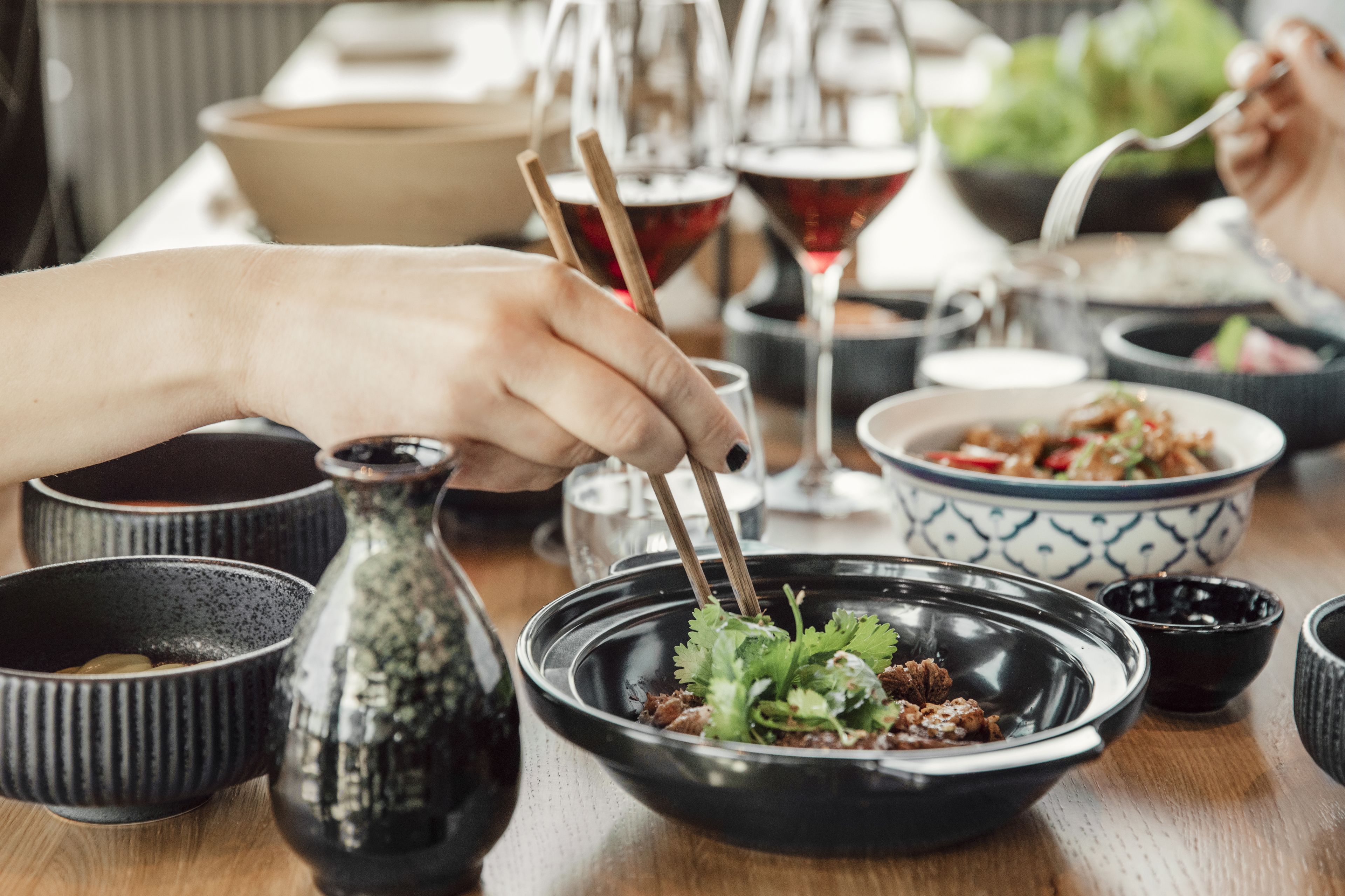 Een eettafel met verschillende schalen eten, stokjes en een wijnglas.