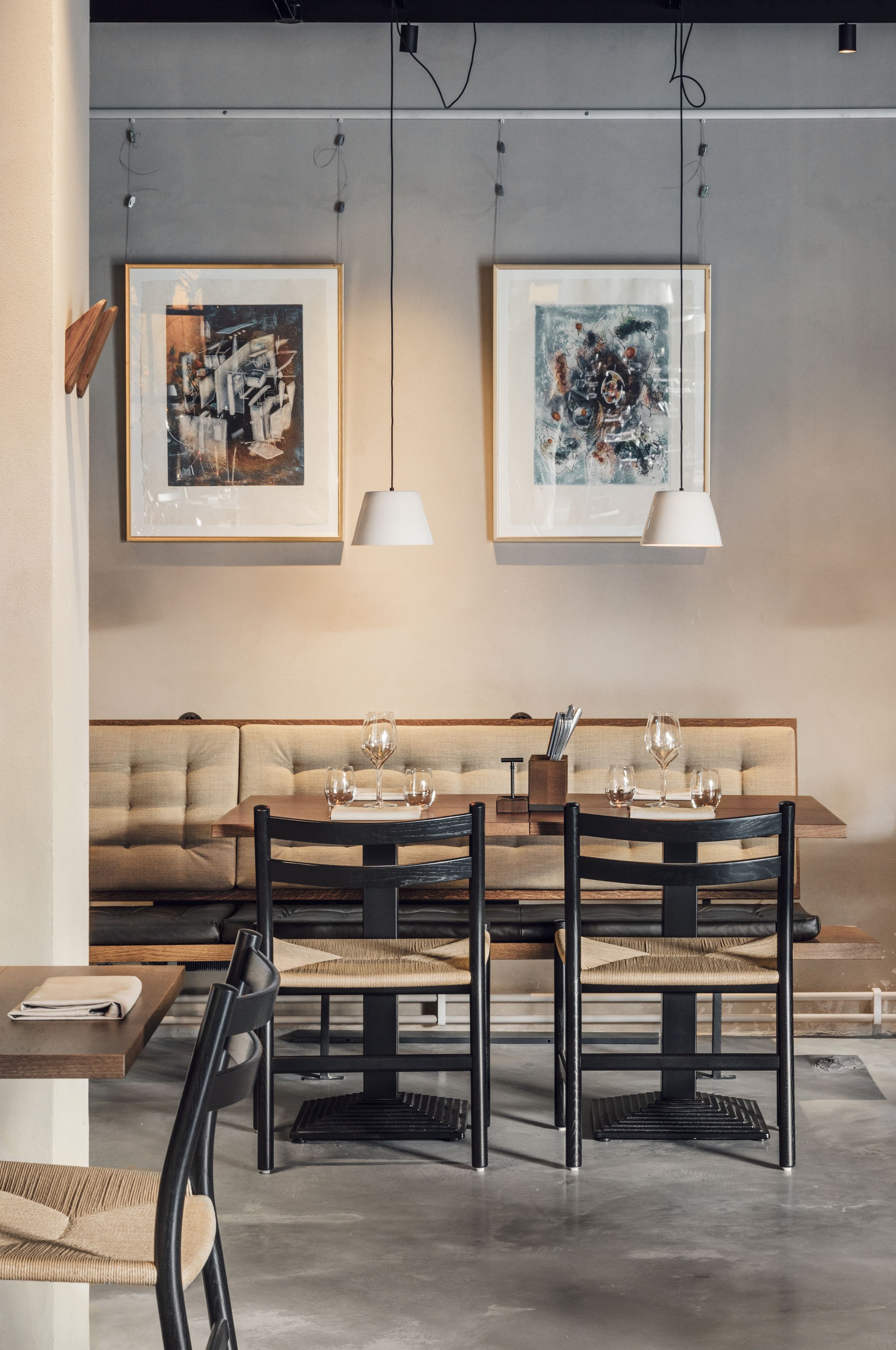 Un moderno comedor con una mesa de madera, sillas negras y un sofá color beige. Dos cuadros enmarcados cuelgan de la pared sobre la mesa.