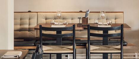 Un moderno comedor con una mesa de madera, sillas negras y un sofá color beige. Dos cuadros enmarcados cuelgan de la pared sobre la mesa.