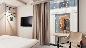 Une chambre d’hôtel avec un lit, une chaise, une télévision et une grande fenêtre avec des rideaux.