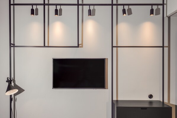 A modern room with a flat-screen TV mounted on the wall, a black floor lamp, and a black cabinet. - Blique by Nobis, Stockholm, a Member of Design Hotel (Stockholm)