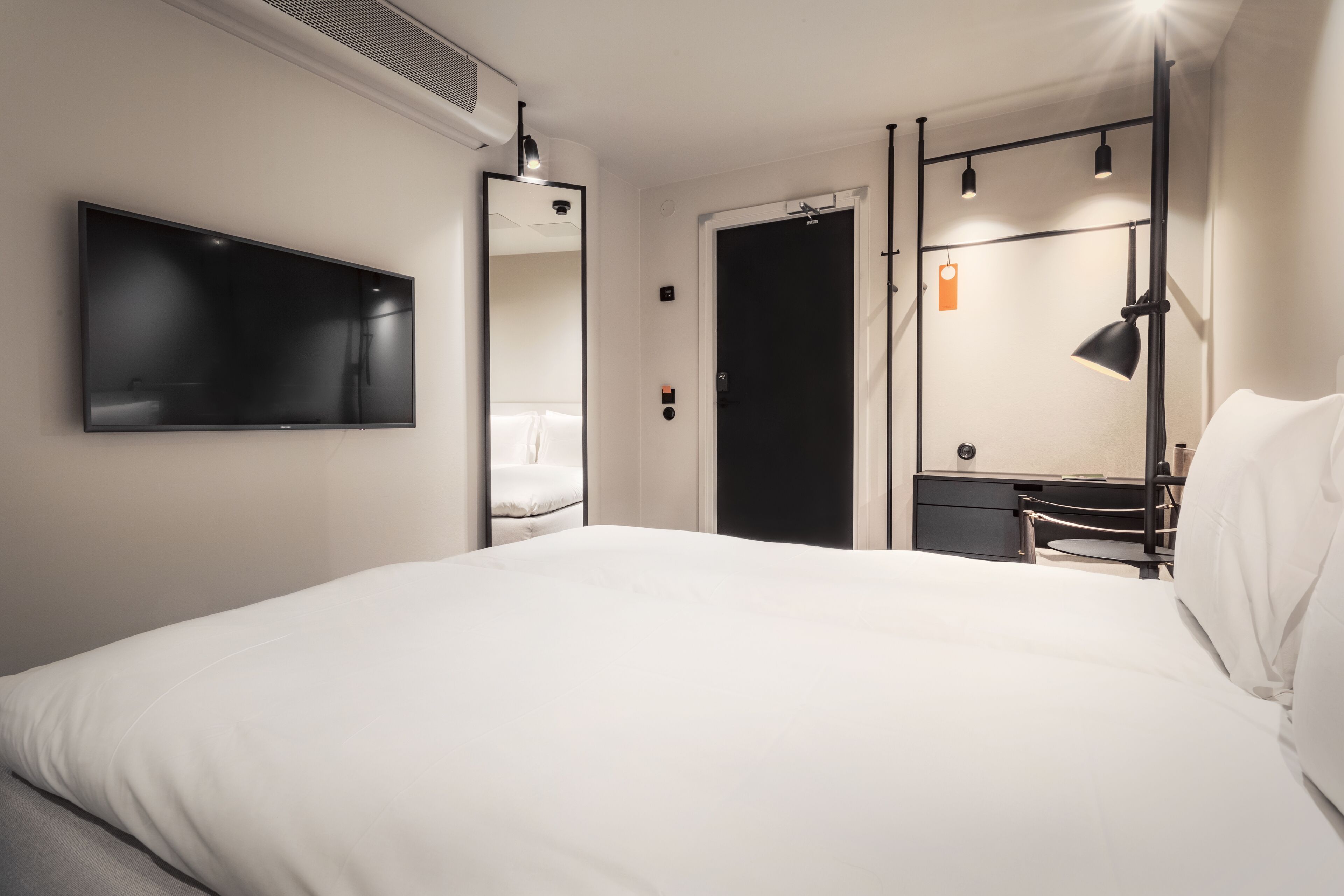 Een moderne hotelkamer met een groot bed, een flatscreen-televisie aan de muur, een bureau met een stoel, en een deur die leidt naar een andere kamer.