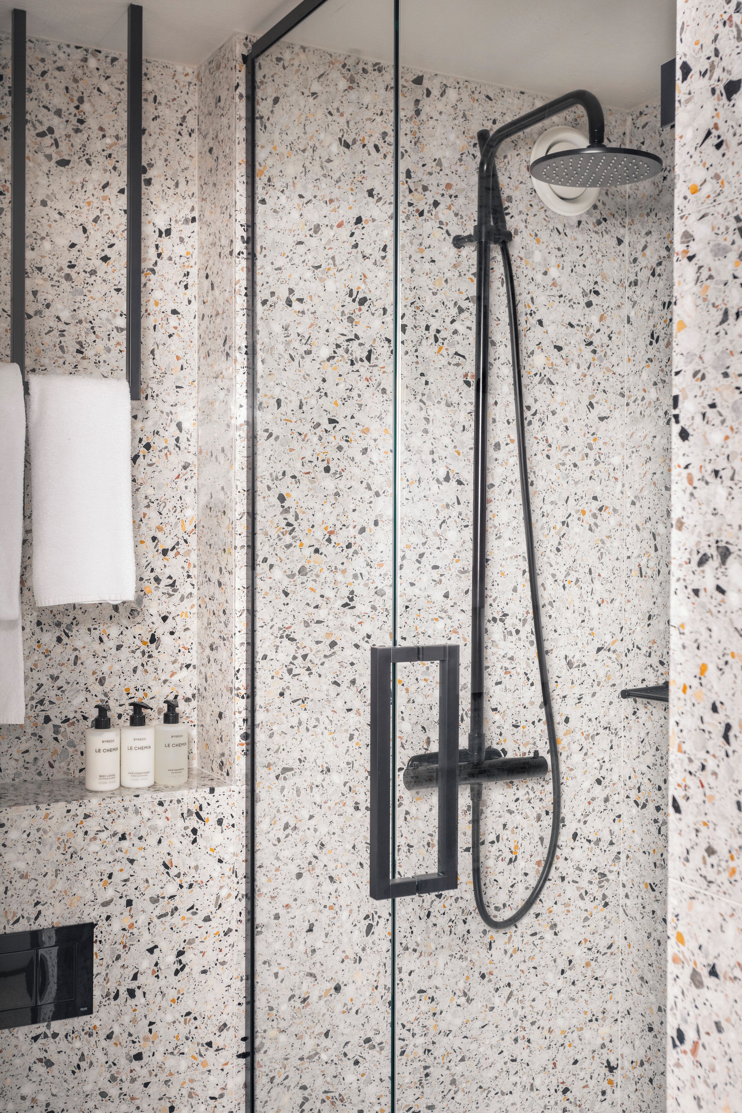 Een moderne badkamer met een betegelde wand met stroomdesign, een douchecabine van glas en een zwarte handdoekhouder met een witte handdoek.