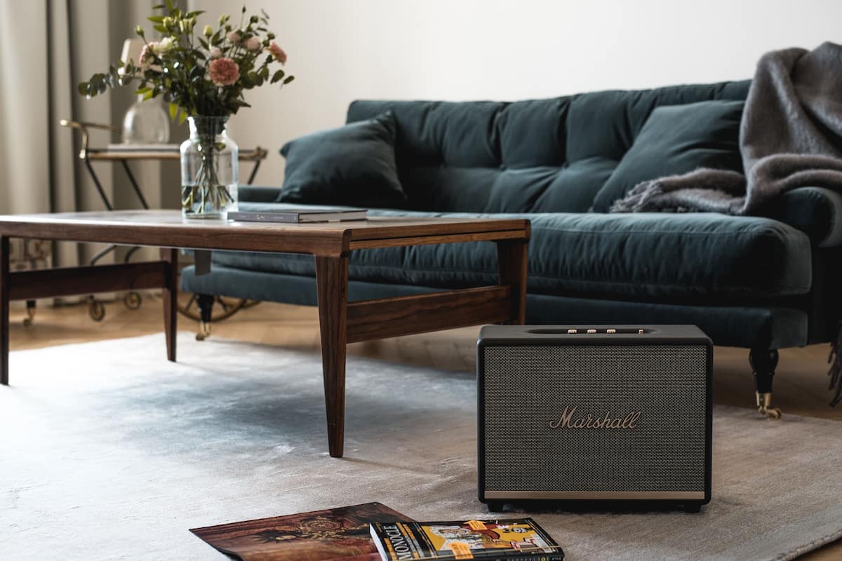 Ein Wohnzimmer mit einem dunkelgrünen Sofa, einem Holztisch, einer Marshall-Anlage und einer Vase mit Blumen.
