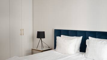Una cama bien hecha con sábanas y toallas blancas, un cabecero azul oscuro y una mesita de noche con una lámpara.