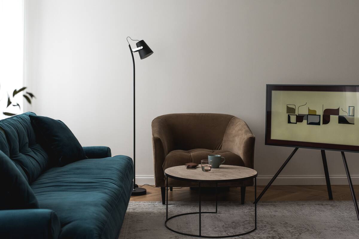Ein modernes Wohnzimmer mit einem petrolfarbenen Sofa, einem braunen Sessel, einem Couchtisch, einer Stehlampe und einem gerahmten abstrakten Kunstwerk an der Wand.