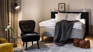 Habitación de hotel con cama, una silla, una mesita con un florero y una lámpara.