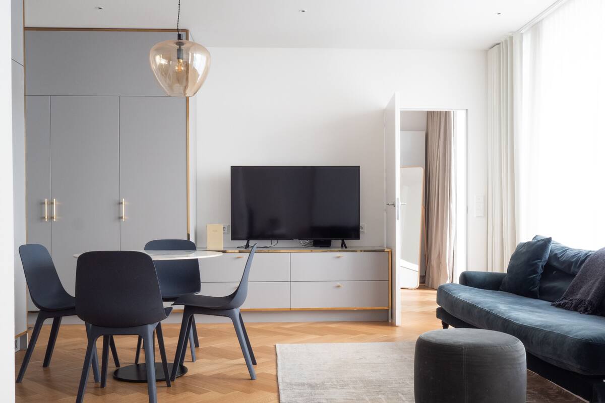 Ein modernes Wohnzimmer mit einer Couch, einem Hocker und einem Essbereich mit Stühlen und einem Tisch.