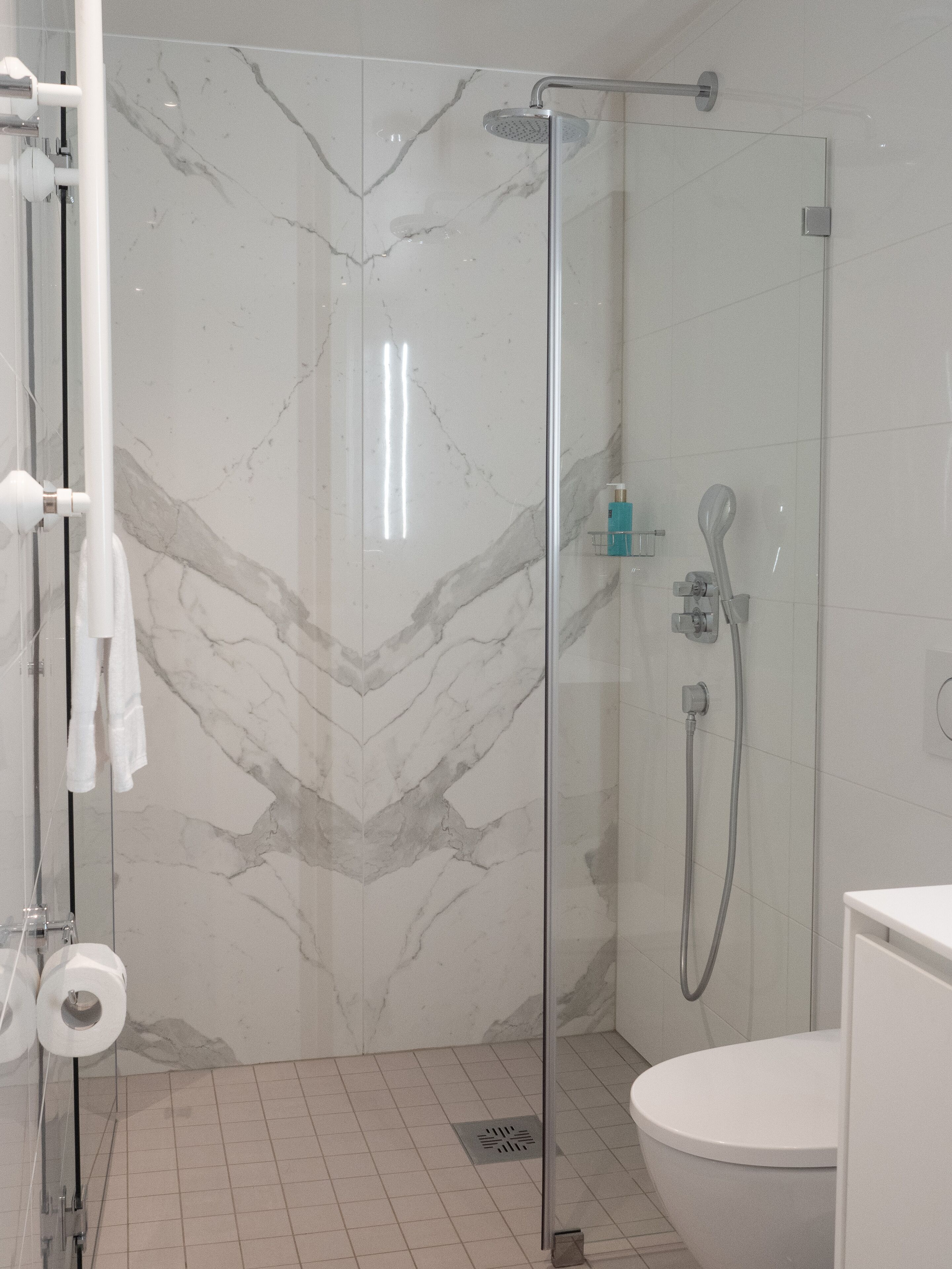 Un baño moderno con ducha envuelta en vidrio, inodoro blanco y paredes con diseño de mármol.