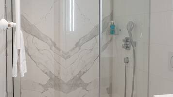 Un baño moderno con ducha envuelta en vidrio, inodoro blanco y paredes con diseño de mármol.