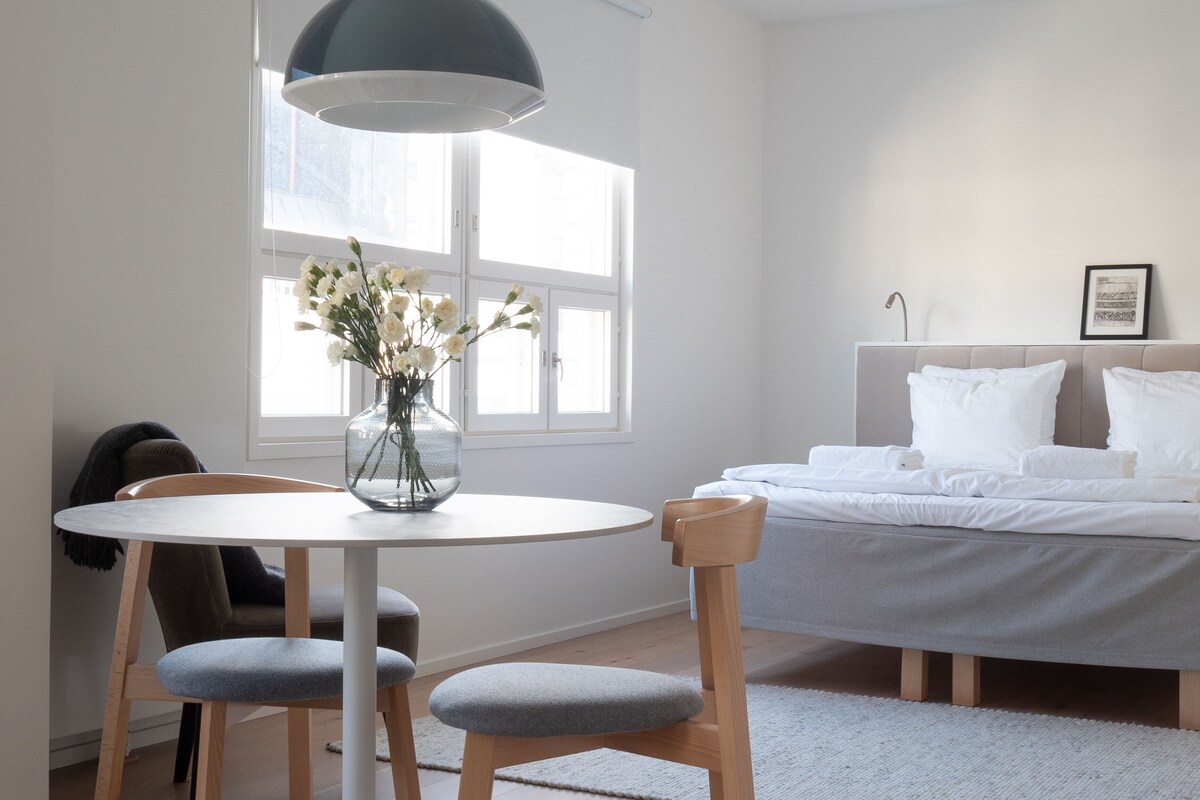 A modern bedroom with a bed, a bedside table, a chair, a window, and a hanging light fixture.