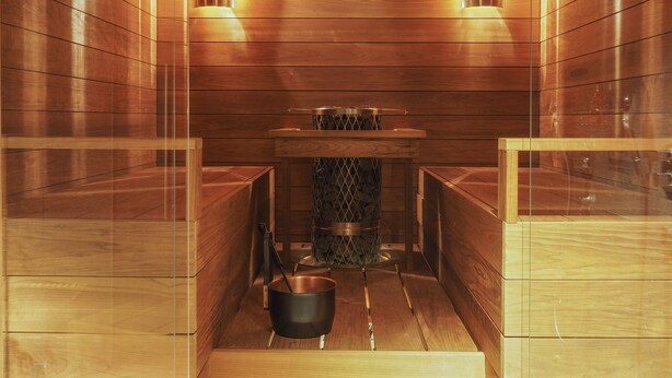 A sauna with wooden walls and benches, a central heating element, and two wall-mounted lights. - Bob W Helsinki Ullanlinna (Helsinki)