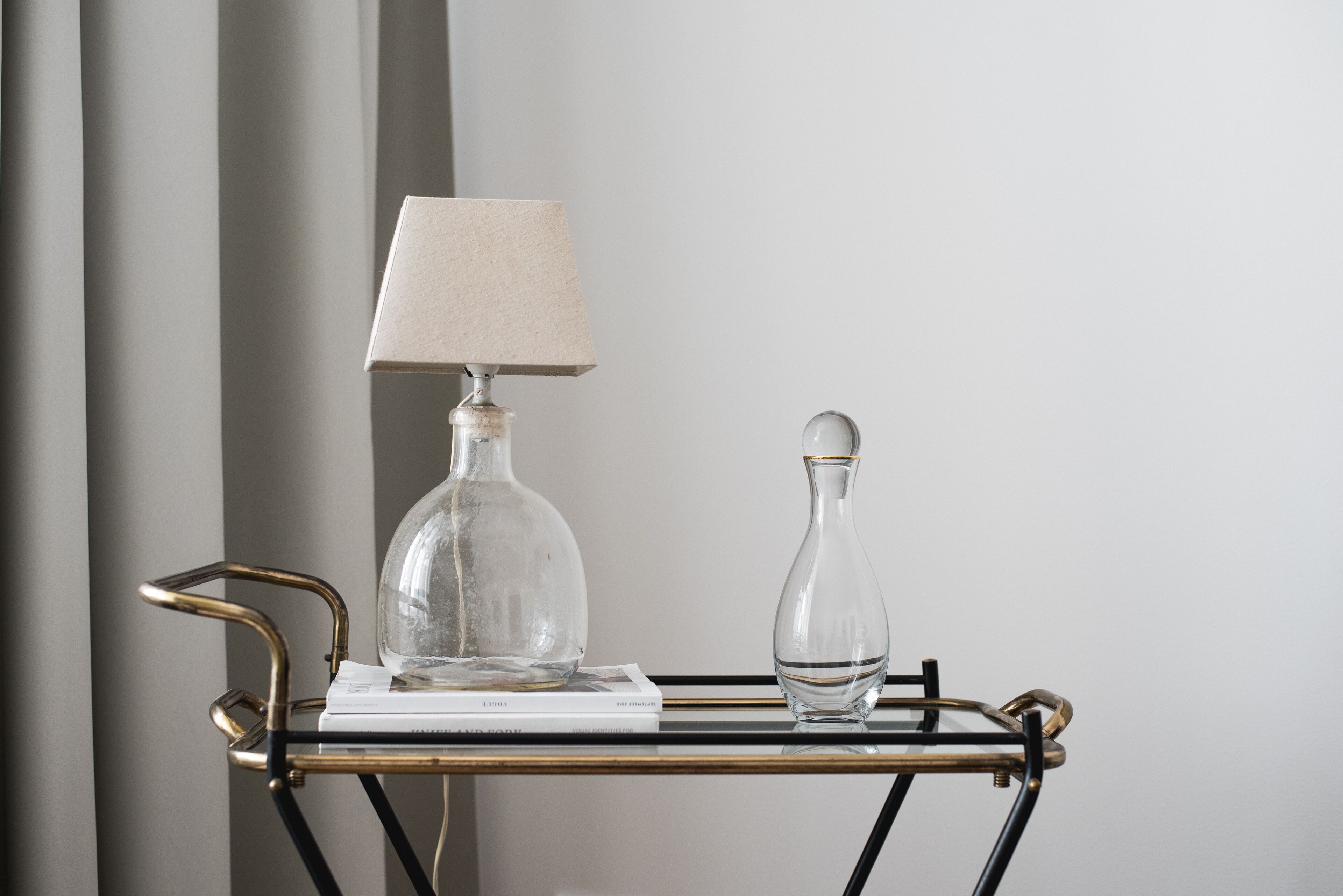 A clear glass lamp and a vase on a metal table with a book.