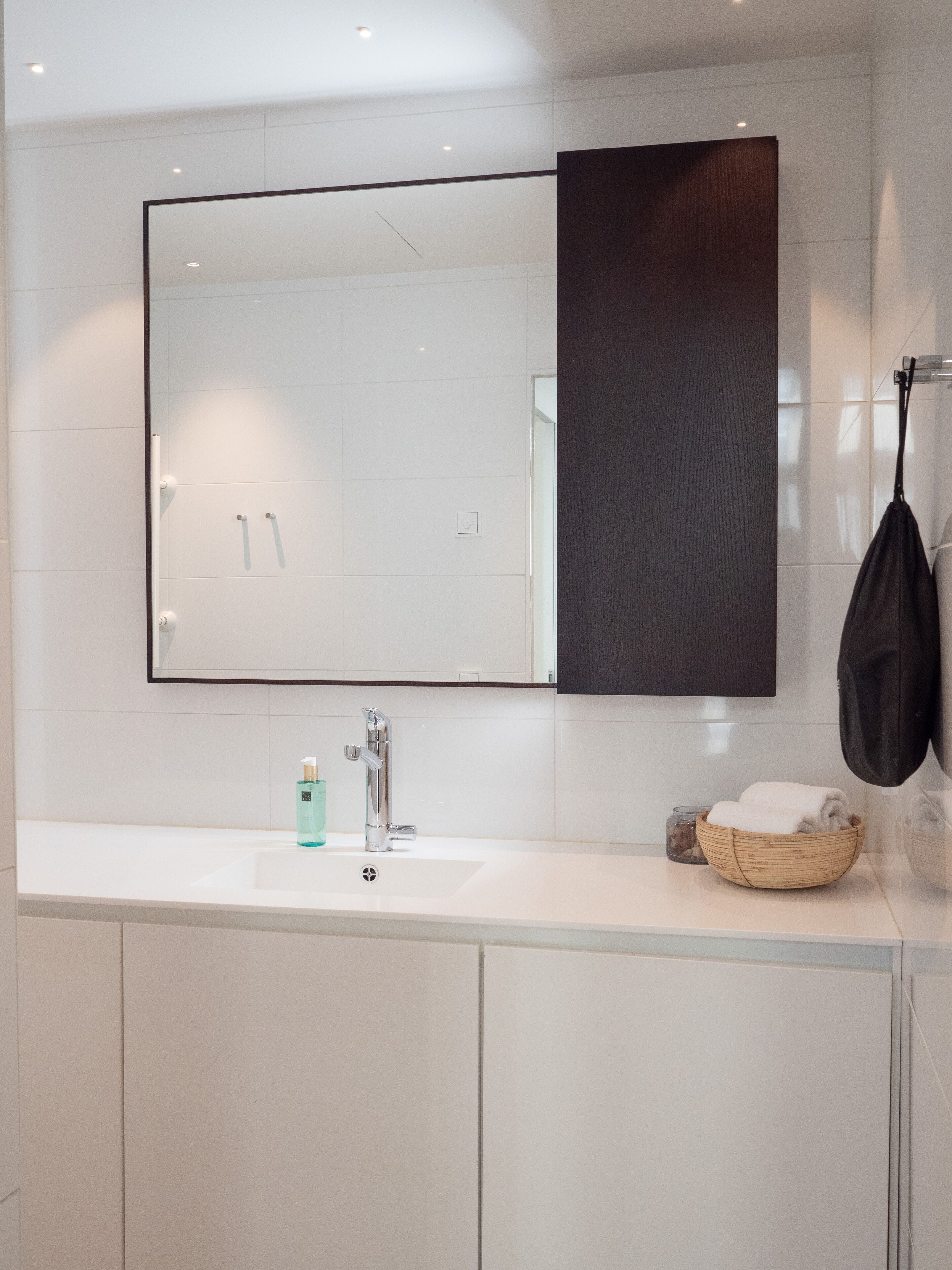 Un baño moderno con un espejo grande, un lavabo blanco y un cuenco de madera con toallas.
