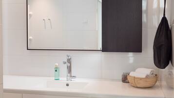 Un baño moderno con un espejo grande, un lavabo blanco y un cuenco de madera con toallas.