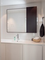 Un baño moderno con un espejo grande, un lavabo blanco y un cuenco de madera con toallas.