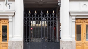 A building entrance with a black wrought iron gate, a white facade, and two wooden doors. - Bob W Helsinki Ullanlinna (Helsinki)
