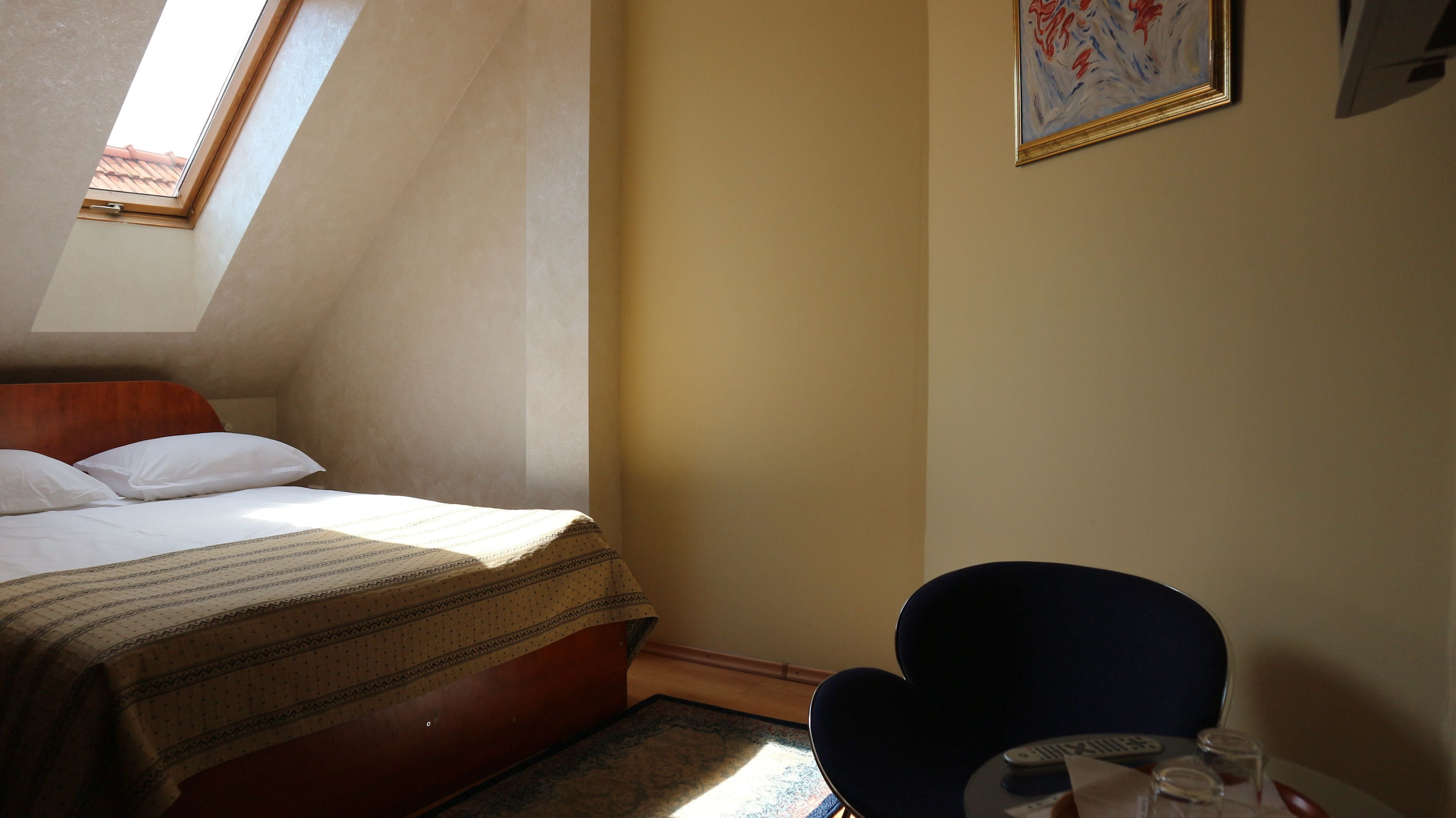 Una habitación de hotel con una cama, una silla, una mesita y un cuadro en la pared.