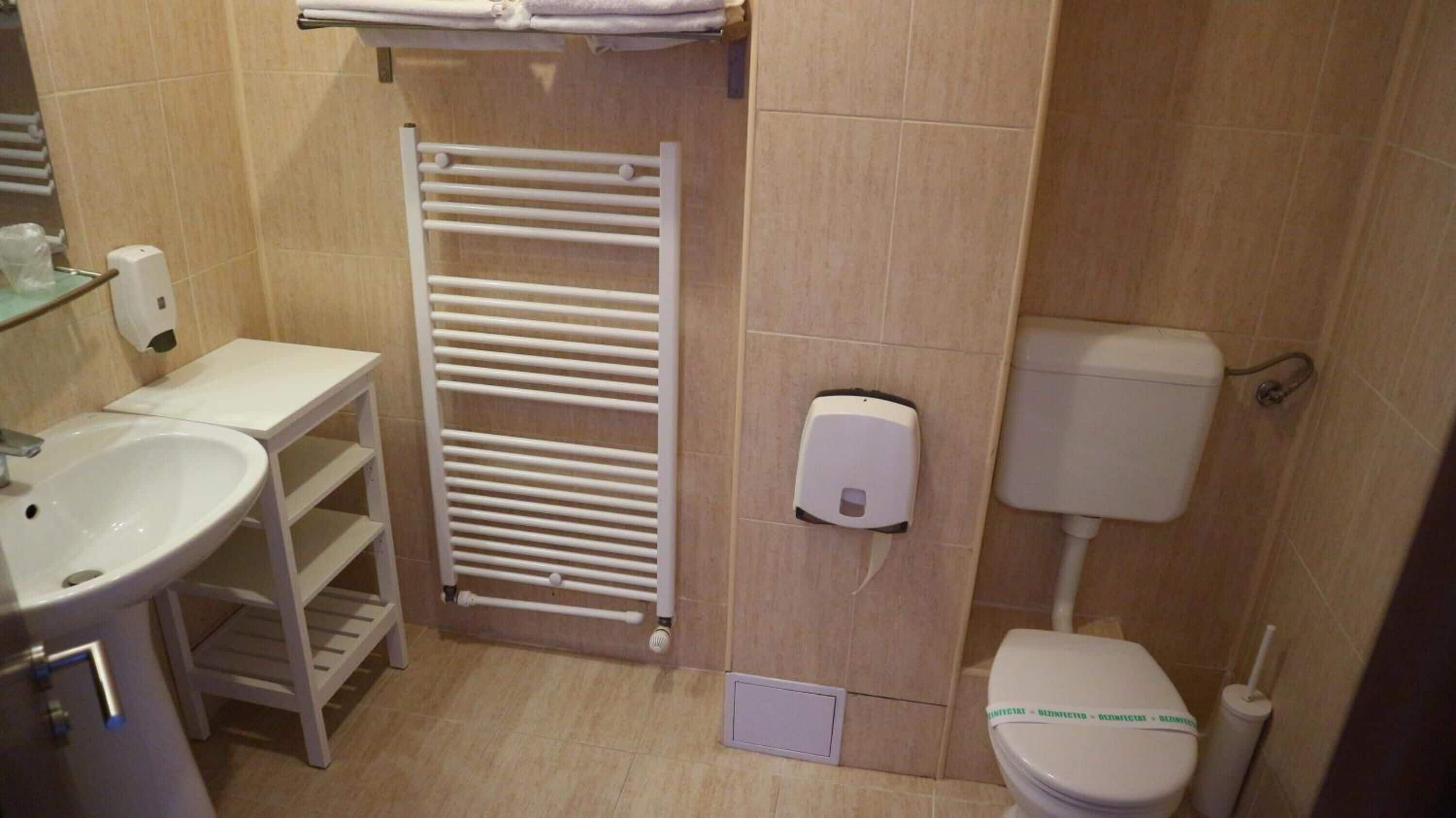 Un baño pequeño con un lavamanos blanco, un perchero para toallas, un inodoro y un dispensador de jabón.