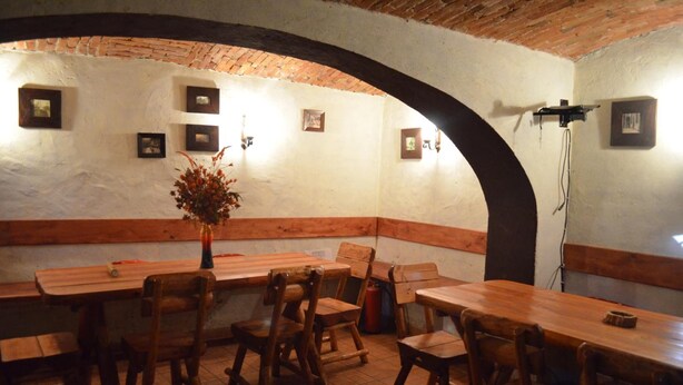 Un coin repas rustique avec des tables et des chaises en bois, un plafond en briques et des tableaux encadrés accrochés aux murs.