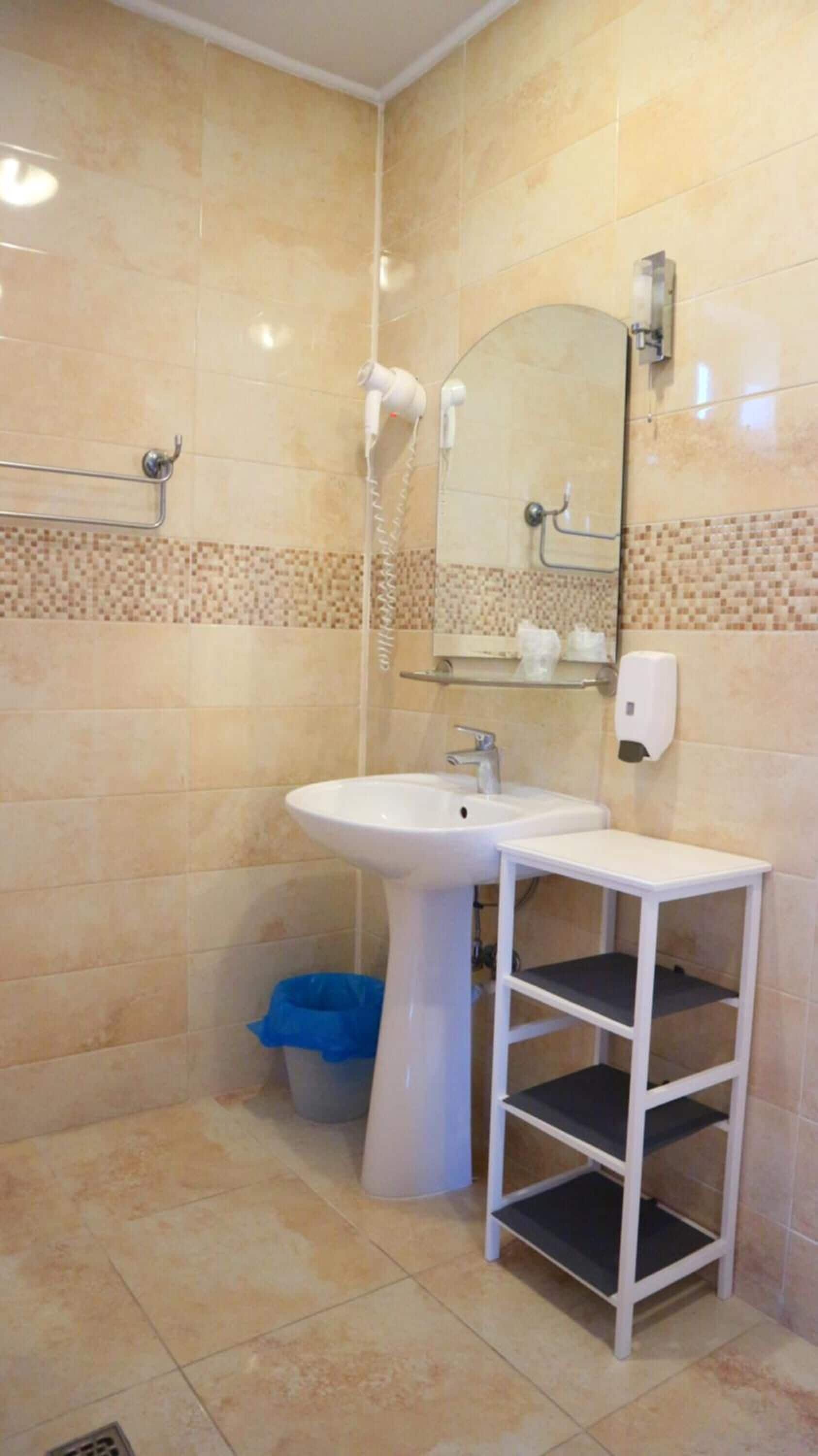 Un baño con un lavabo blanco, un espejo, un perchero para toallas y una ducha.