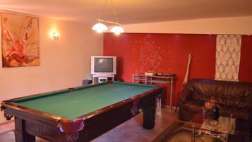 A pool table in a room with a red wall, a television, and a leather couch.