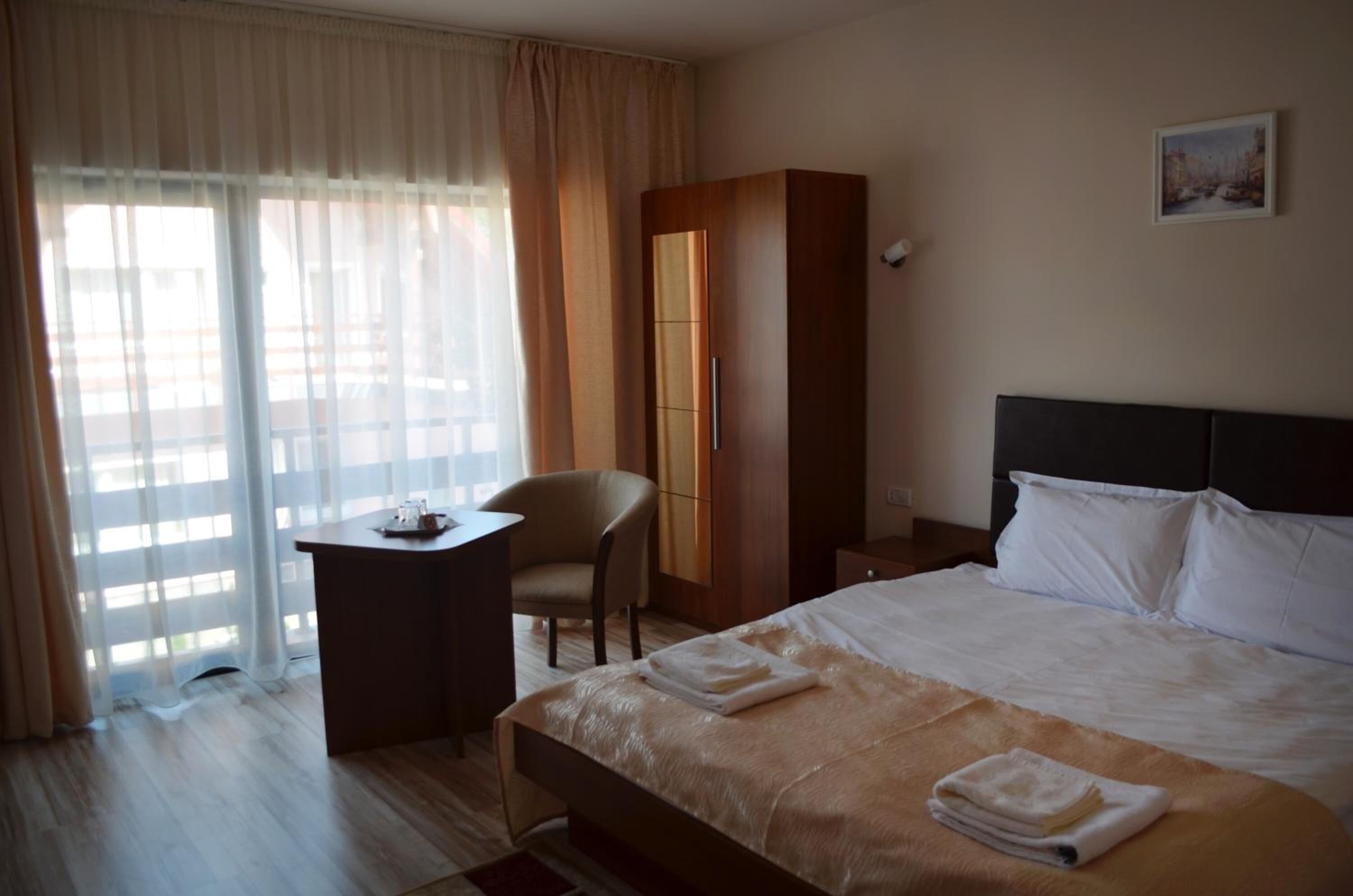 Quarto de hotel com uma cama, uma escrivaninha, uma cadeira e um guarda-roupa.