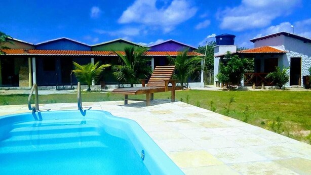 A swimming pool with lounge chairs, a covered patio area, and a building with a tiled roof. - Pousada Delicia de Sono (Cajueiro da Praia)