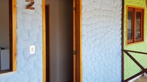 A room with a textured wall, a wooden door, and a window with a wooden frame. - Pousada Delicia de Sono (Cajueiro da Praia)