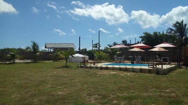 Un patio trasero con piscina, mobiliario exterior y una zona cubierta.