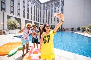 A group of people taking a selfie by a swimming pool with a modern building in the background.