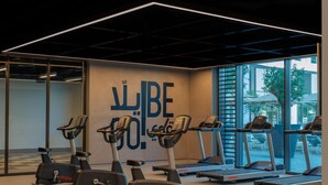 A gym with cardio equipment, a large window, and a motivational wall with Arabic text. - Rove At The Park (Dubai)
