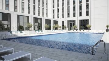 Um edifício moderno com piscina, espreguiçadeiras e plantas em vasos.