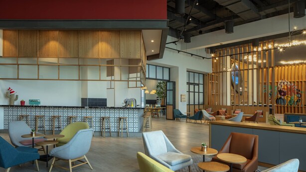 A modern interior with a bar area, seating with round tables, and a wooden accent wall. - Rove At The Park (Dubai)