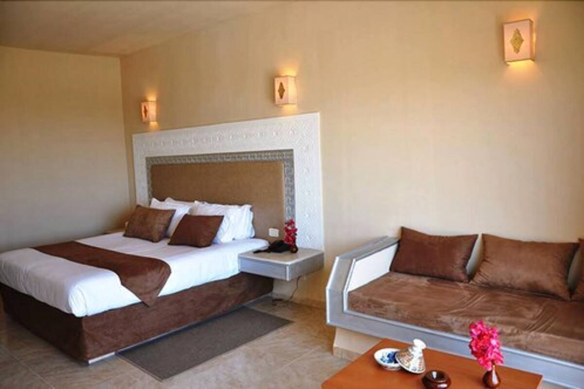 Une chambre d’hôtel avec deux lits, un canapé, une table de chevet et une petite table sur laquelle se trouve un vase.