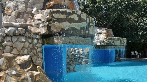 A pool with a stone waterfall feature and a stone wall. - Hôtel Narcis - Adults Only (Nabeul)