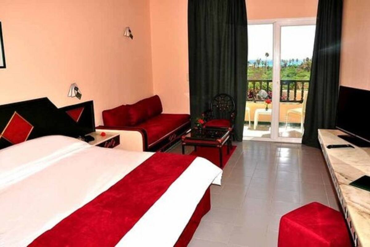 Une chambre d’hôtel avec un grand lit, un canapé rouge, une petite table et un balcon avec vue.