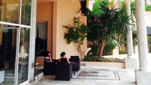 A spacious indoor area with a large chandelier, glass doors, and a seating area with two people. - Hôtel Narcis - Adults Only (Nabeul)