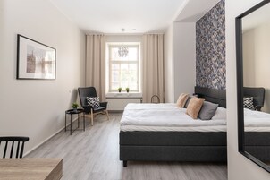 Un dormitorio moderno con una cama grande, una silla, una mesita y un ventanal con cortinas.
